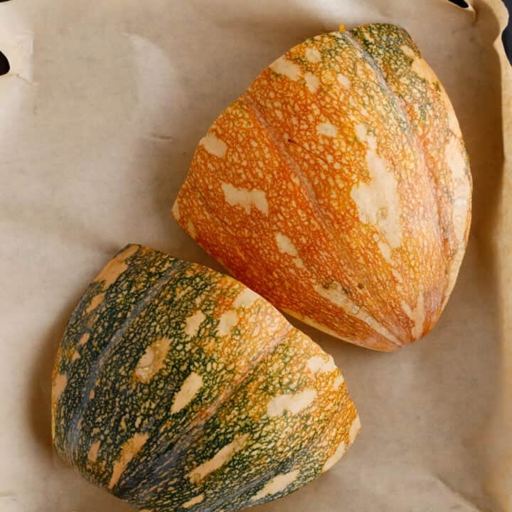 Two pumpkin wedges with orange and green mottled skin rest on parchment paper, ready to be transformed into smooth pumpkin puree.