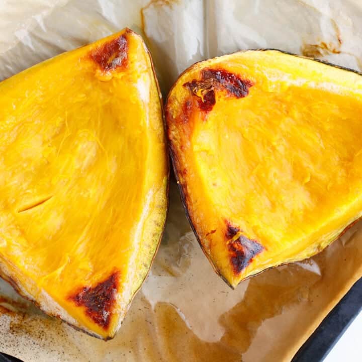 Two roasted kabocha squash halves with golden, slightly caramelized edges on parchment paper&mdash;perfect for scooping out and making smooth pumpkin puree.