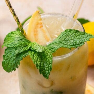 A refreshing guava lemonade garnished with mint leaves and a guava slice, with lemons in the background.