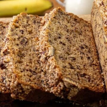 Close-up of sliced banana bread with a crumb topping on a wooden cutting board, bananas in the background.