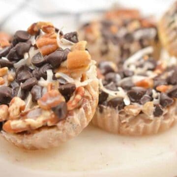 Three nut and chocolate chip clusters on a white cutting board, topped with shredded coconut.