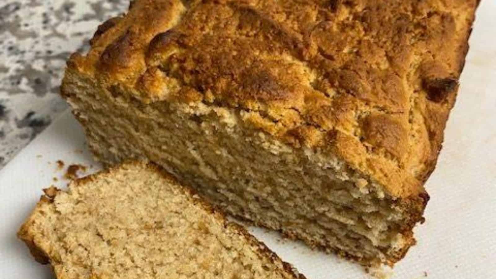 Loaf of peanut butter bread with one cut slice on white cutting board.