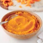 A bowl of smooth, velvety pumpkin puree with a spoon resting inside.