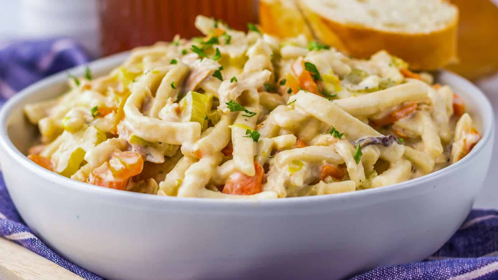 A bowl of creamy chicken noodle casserole with vegetables, garnished with parsley.
