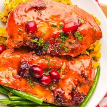 Glazed chicken breasts with cranberries, green beans, and stuffing on a white plate, garnished with parsley.