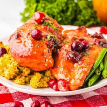 Plate of glazed chicken with cranberries, green beans, and stuffing on a red checkered tablecloth.