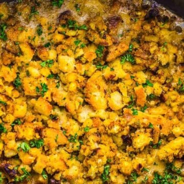 Golden-brown stuffing topped with chopped herbs, baked until crispy in a black dish.