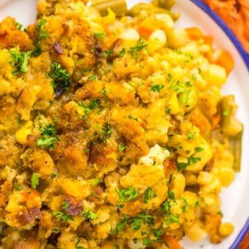 A plate of vegetable casserole topped with golden stuffing and garnished with chopped parsley.