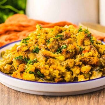 A plate of cornbread stuffing with herbs on a wooden table, with an orange cloth in the background.
