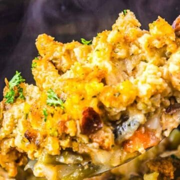 A spoonful of cheesy casserole with vegetables and herbs, lifted from a baking dish.