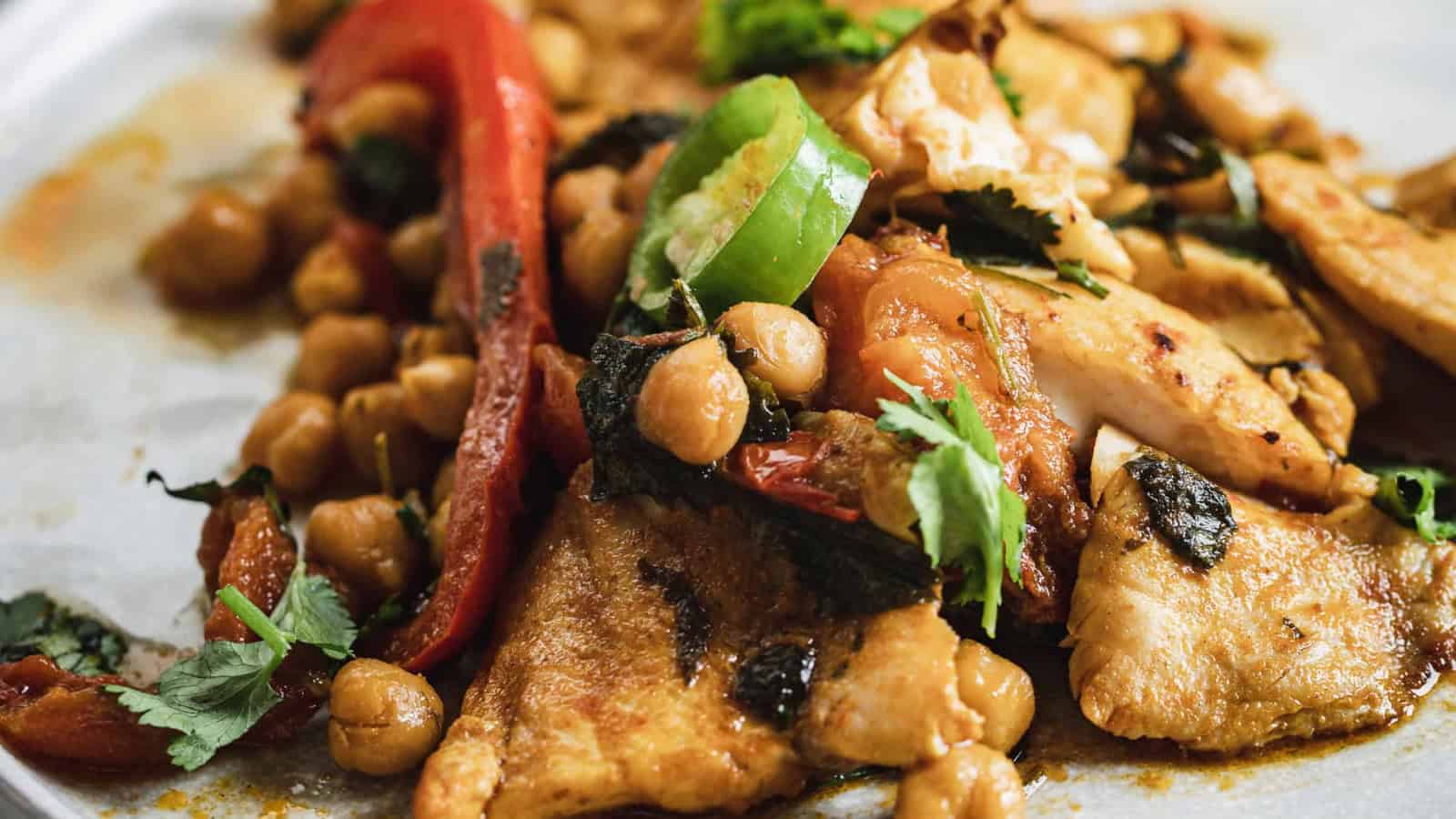 A cooked fish with chickpeas, tomatoes, green pepper, and herbs in a savory sauce.