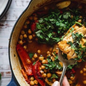 A fork holds a bite of chickpea stew with herbs above a pot filled with stew, chickpeas, and greens.