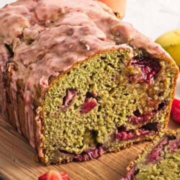 Sliced loaf of strawberry banana bread on a wooden board, surrounded by fresh strawberries and bananas.
