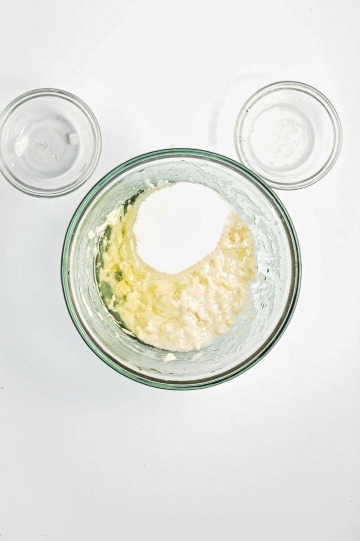 A bowl with mashed bananas and sugar, flanked by two smaller bowls on a white surface.