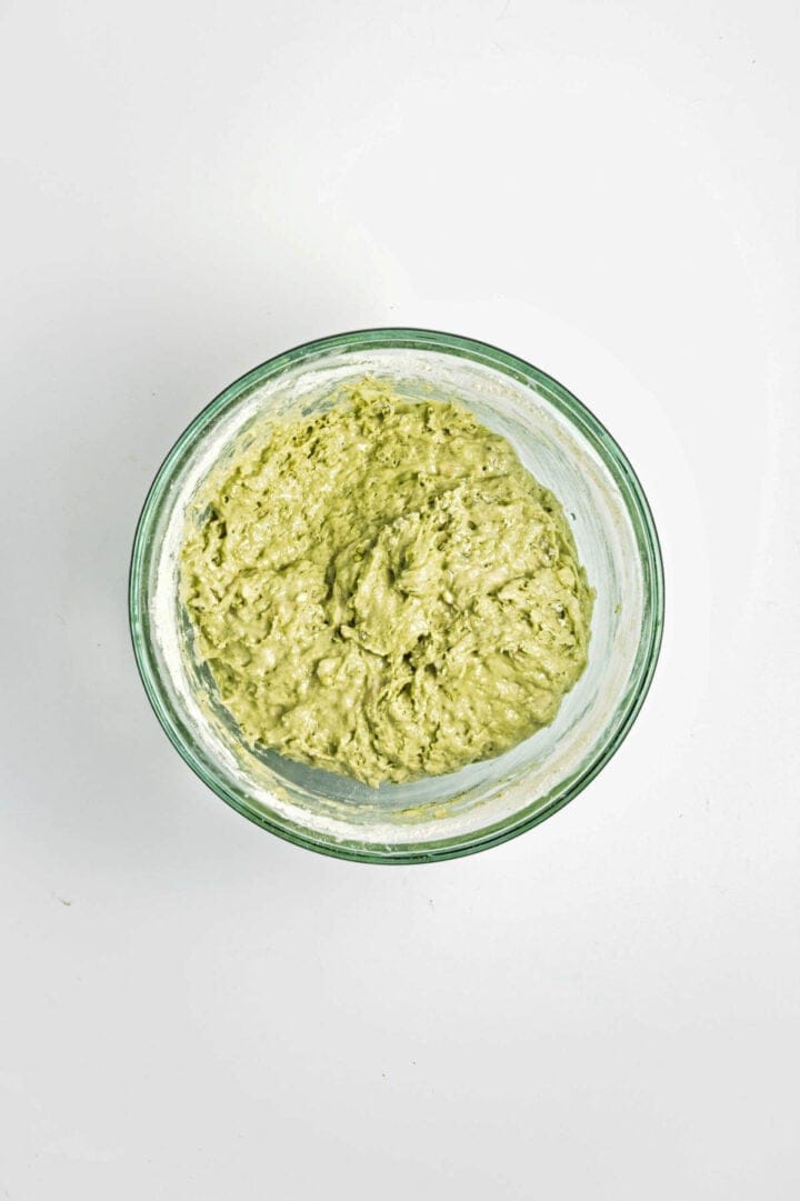 A glass bowl filled with thick, light green batter on a white background.