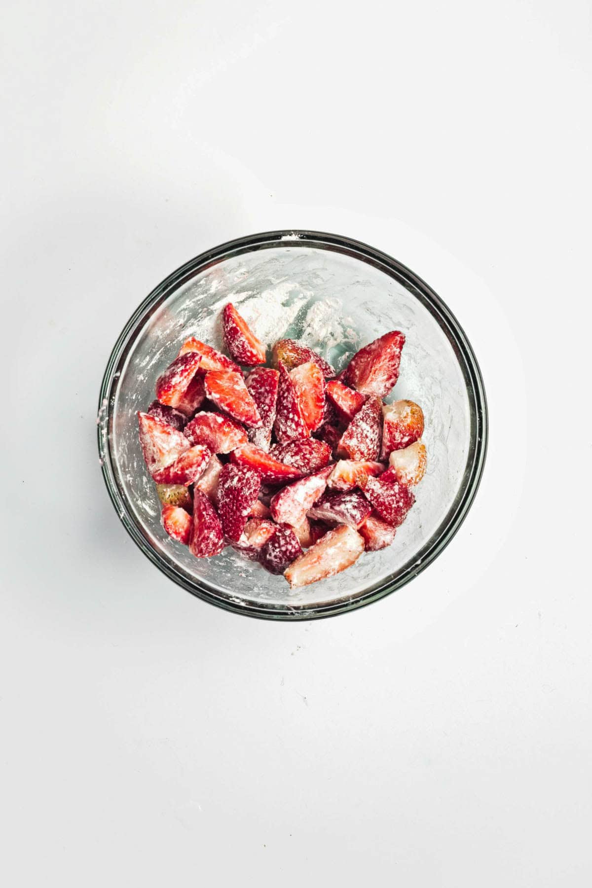 Sliced strawberries coated with sugar in a clear glass bowl on a white background.