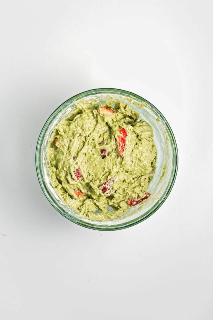 Bowl of guacamole with visible chunks of tomato and onion, on a white background.