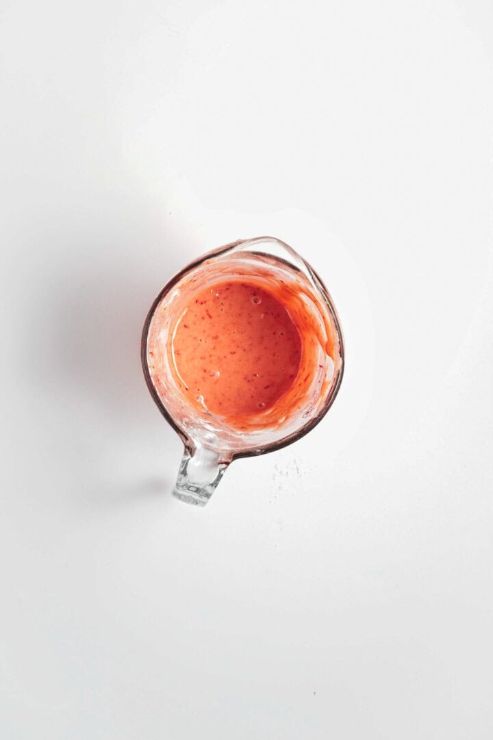 Glass measuring cup filled with pink smoothie on a white background, viewed from above.