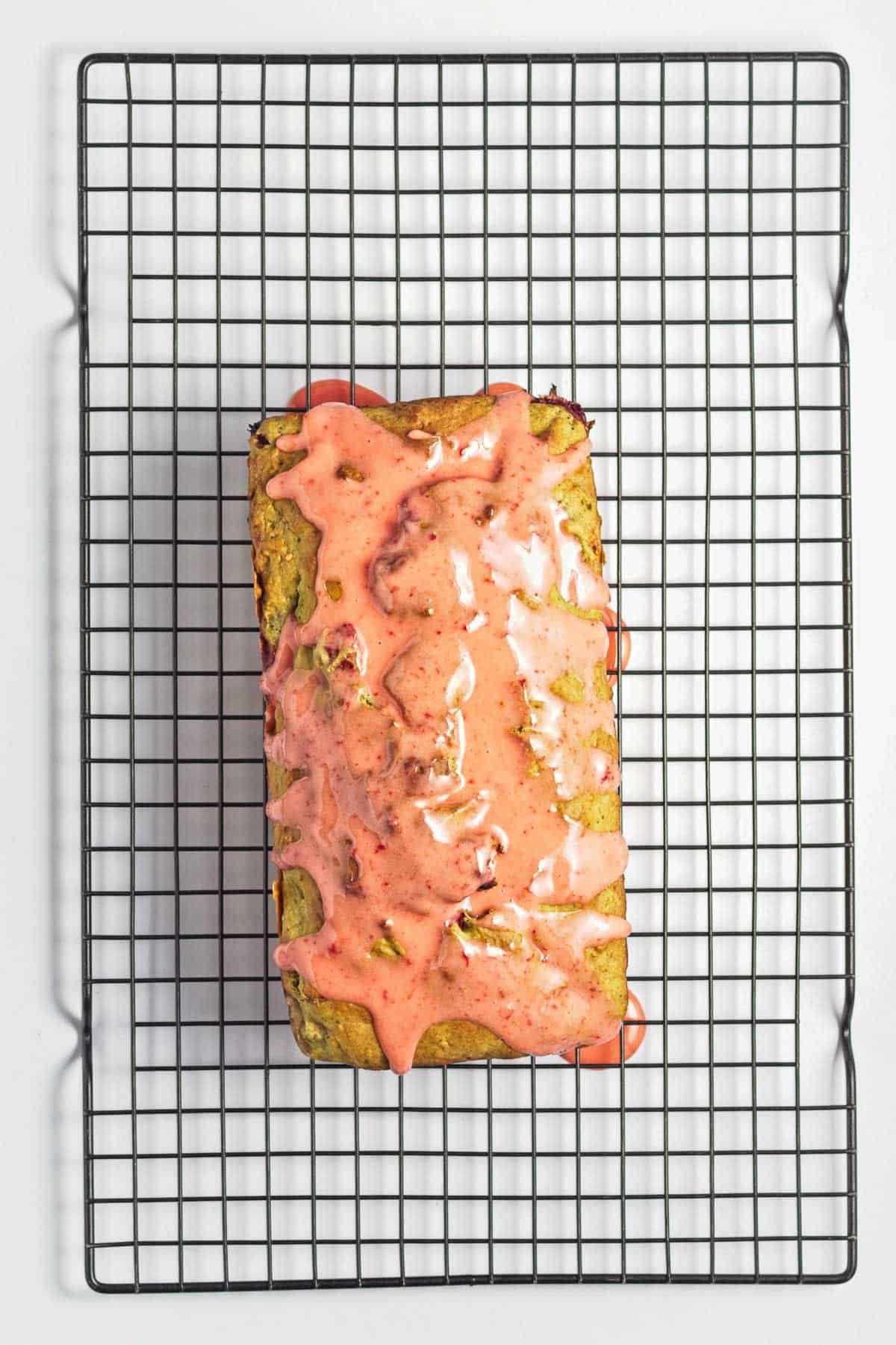 Loaf of bread with pink glaze on top, cooling on a wire rack against a white background.