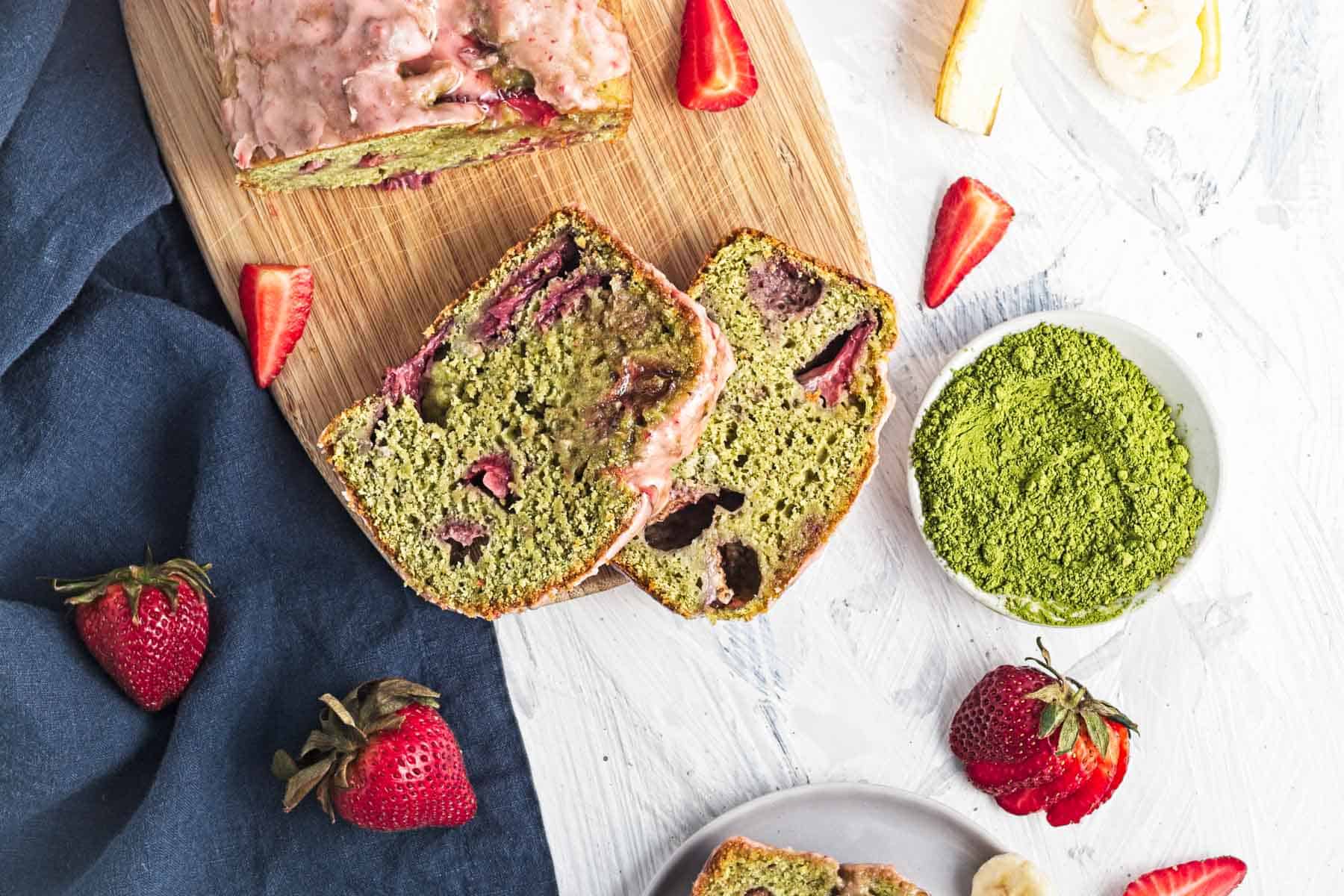Sliced strawberry matcha bread on a cutting board with fresh strawberries and matcha powder nearby.