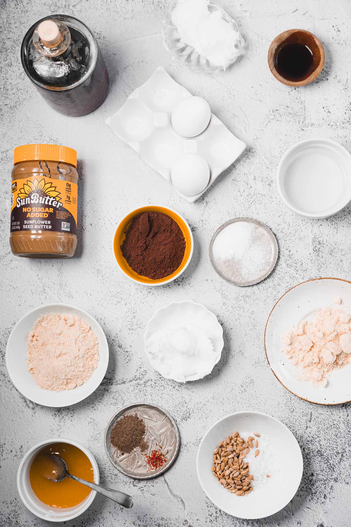 Various baking ingredients, including eggs, cocoa, peanut butter, and spices, arranged on a light countertop.