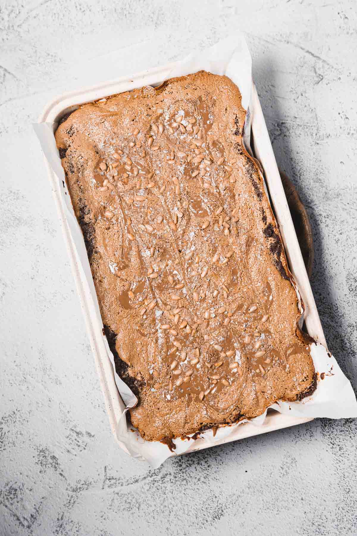 A rectangular chocolate cake in a parchment-lined pan, topped with a dusting of powdered sugar.