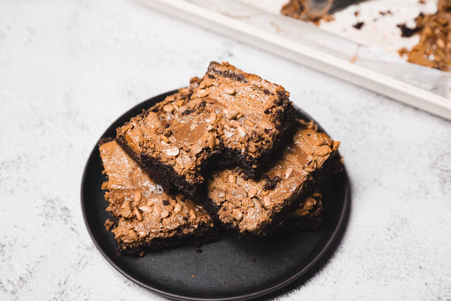 A stack of three chocolate brownies with a crunchy topping on a black plate.