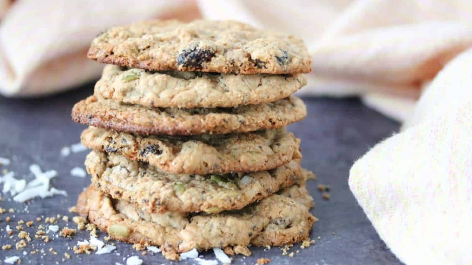 Six trail mix, gluten-free protein cookies stacked on top of one another with coconut around them.