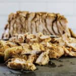 Sliced, seasoned Turkey Shawarma with visible spices and onions on a cutting board, with more meat in the background.