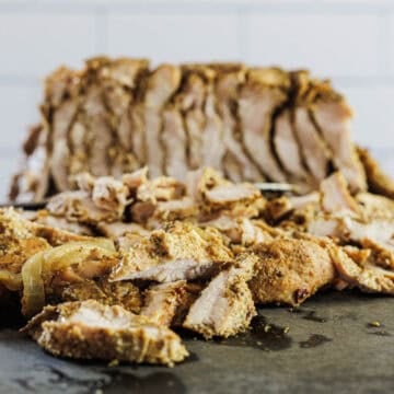 Sliced, seasoned Turkey Shawarma with visible spices and onions on a cutting board, with more meat in the background.