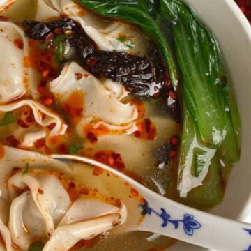 A bowl of spicy noodle soup with bok choy, chili oil, and a ceramic spoon.