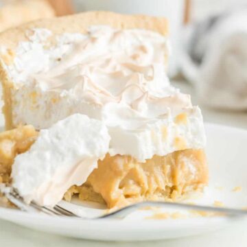 A slice of creamy pie with meringue topping on a white plate, with a fork taking a bite.