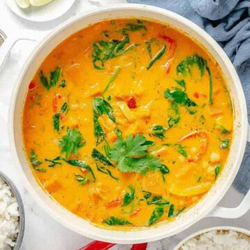 A pot of yellow curry with vegetables and greens, surrounded by bowls of rice and cooking ingredients.