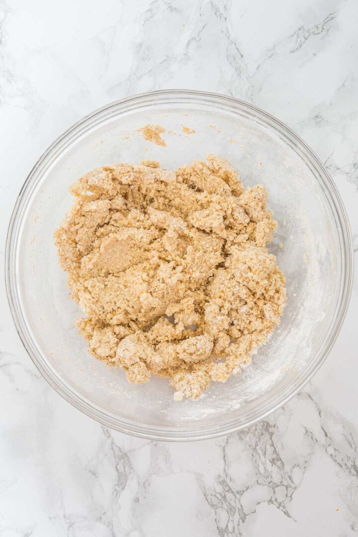 A glass bowl with cookie dough mixture on a white marble surface.