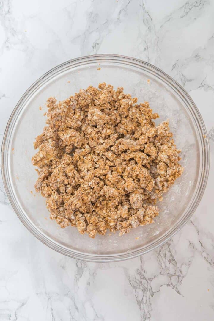 A glass bowl filled with crumbly oat mixture on a marble countertop.