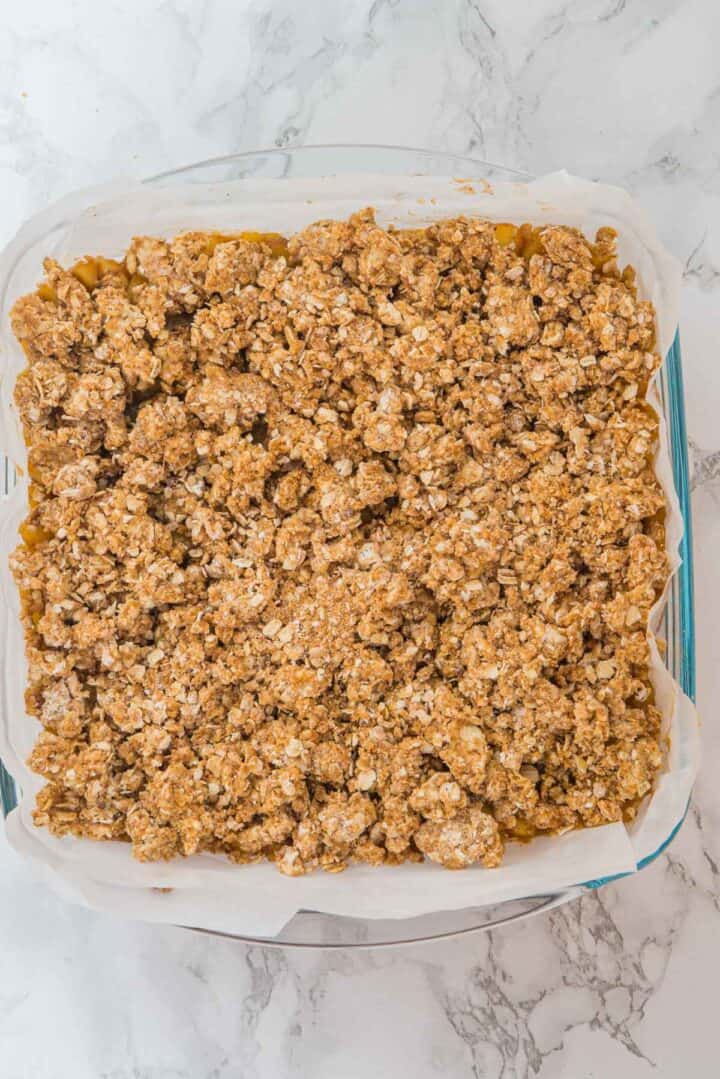A square baking dish filled with golden brown oat crumble on parchment paper, on a marble surface.