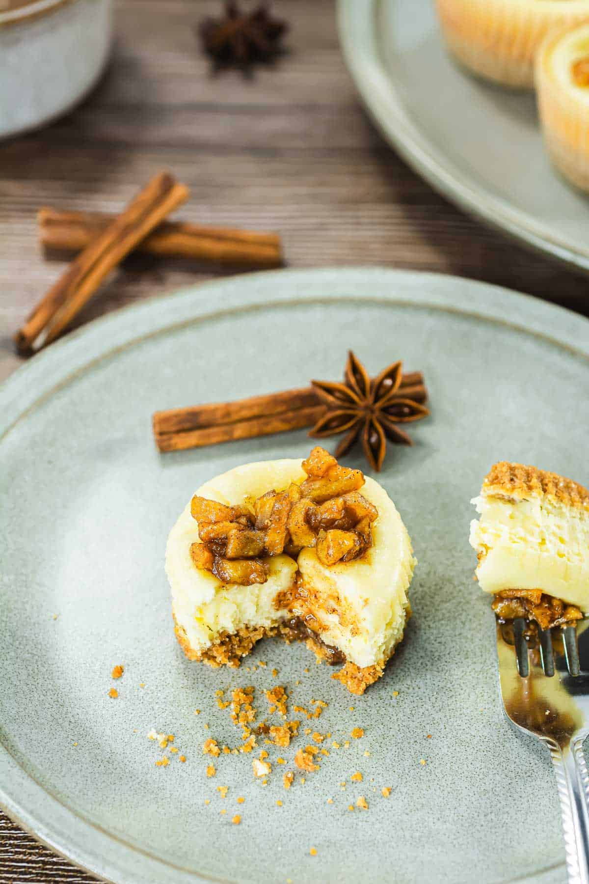 Mini cheesecake topped with spiced apples on a plate, with a cinnamon stick and a star anise beside it.