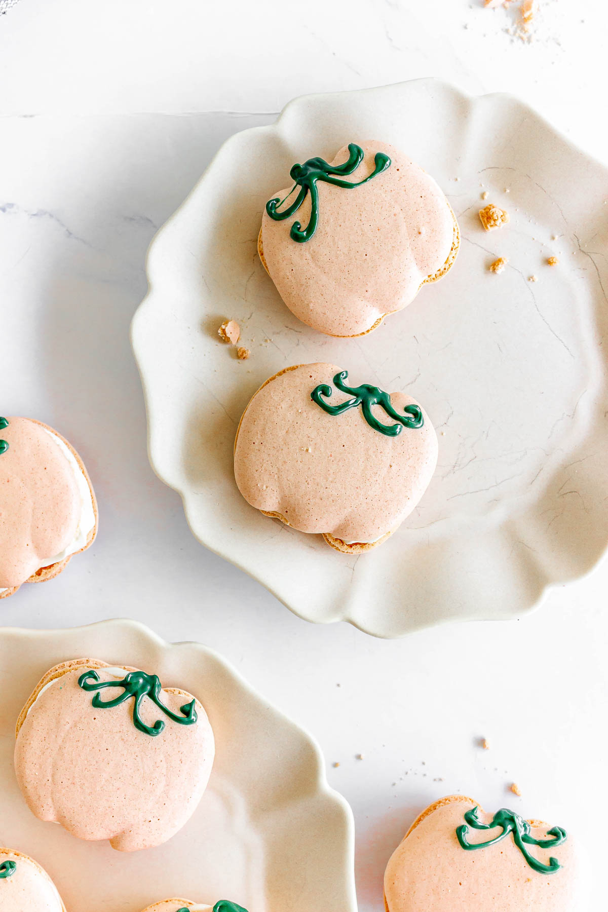 Pumpkin Macarons with green icing stems are arranged on white plates, viewed from above.