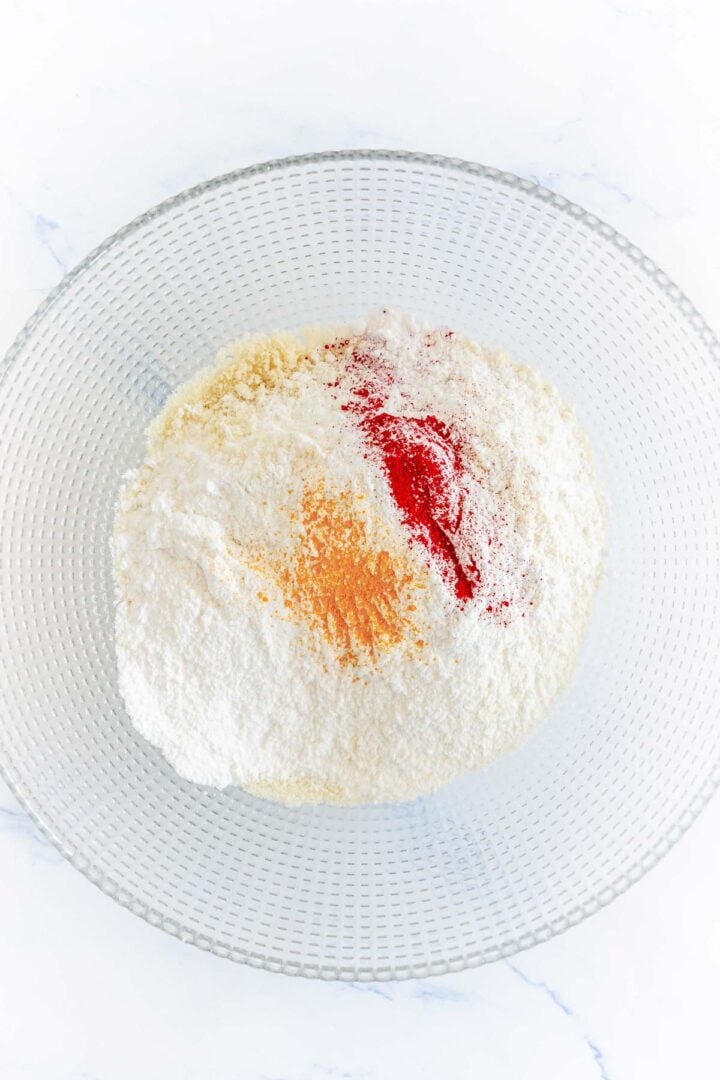 A glass bowl with flour, paprika, and cayenne pepper on a white surface, perfect for adding a hint of spice to your Pumpkin Macarons.