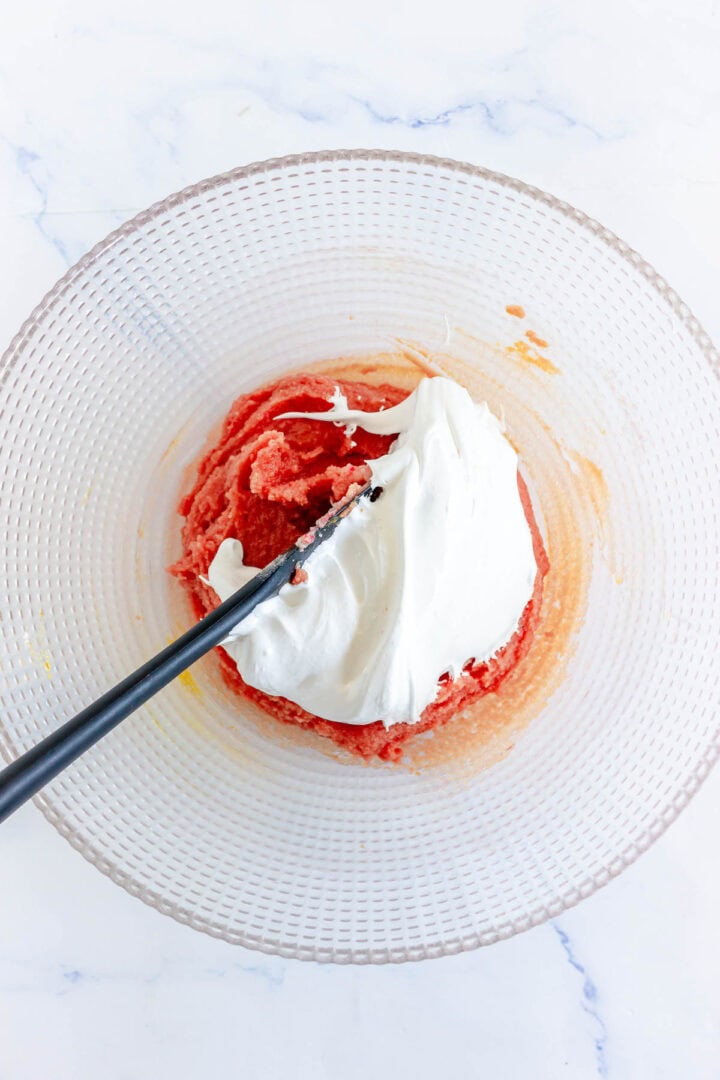 Clear bowl with a pink mixture and white cream being mixed together with a black spatula, preparing a delightful filling for Pumpkin Macarons.