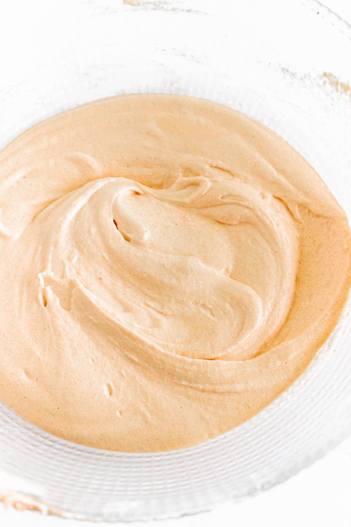 Light orange creamy mixture swirled in a clear glass bowl on a white surface, perfect for filling Pumpkin Macarons.