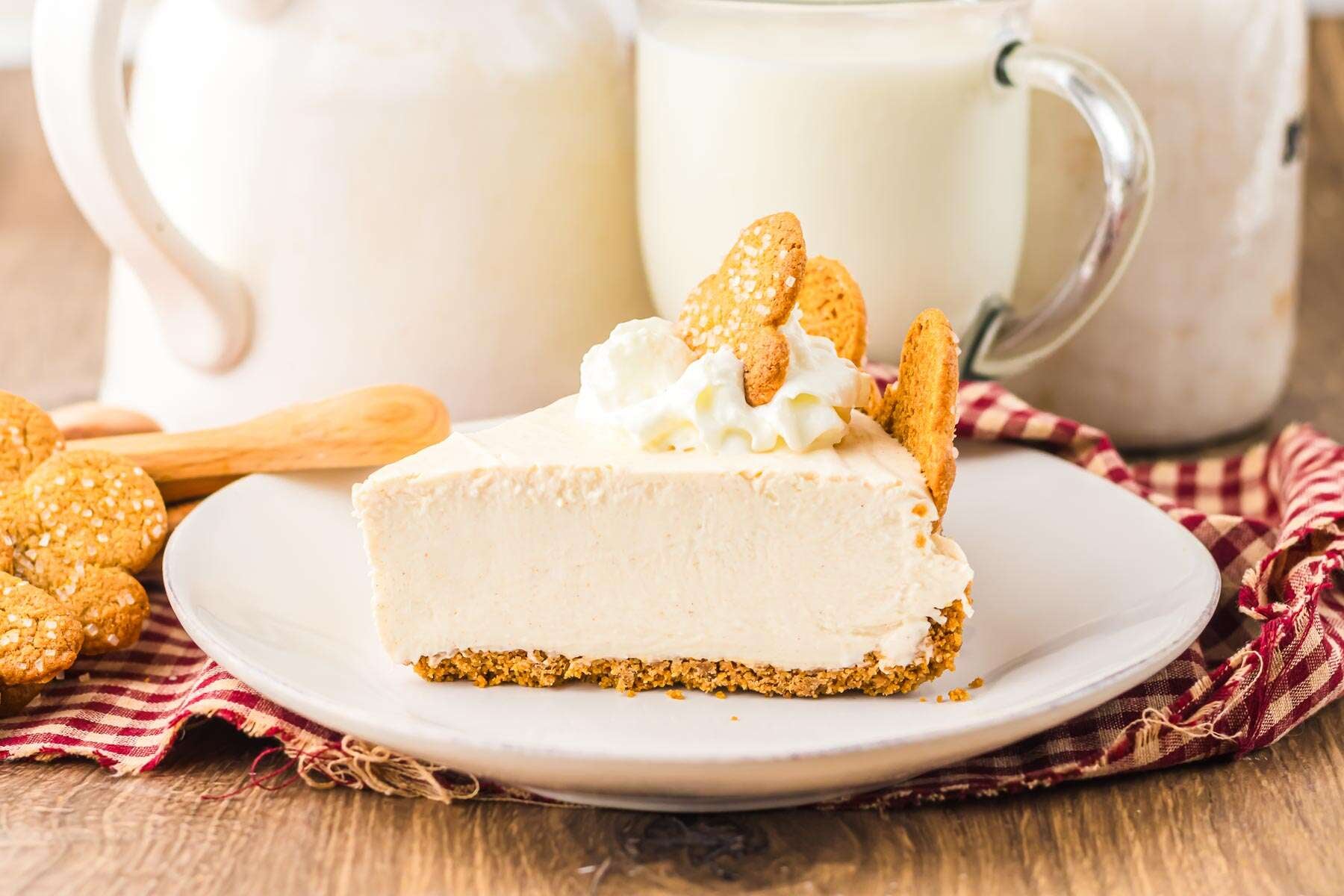 A slice of creamy No Bake Gingerbread Cheesecake with whipped topping and cookies on a plate, with milk in the background.