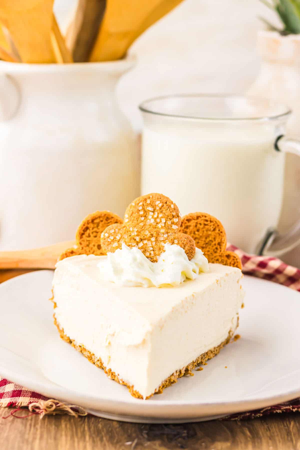 A slice of No Bake Gingerbread Cheesecake topped with whipped cream and gingerbread cookies, served next to a glass of milk.