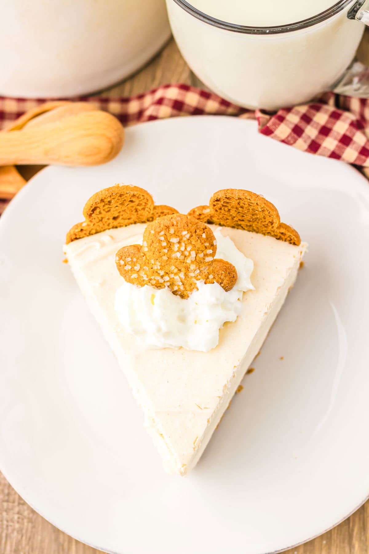 A slice of No Bake Gingerbread Cheesecake topped with whipped cream and three ginger cookies, served on a white plate.