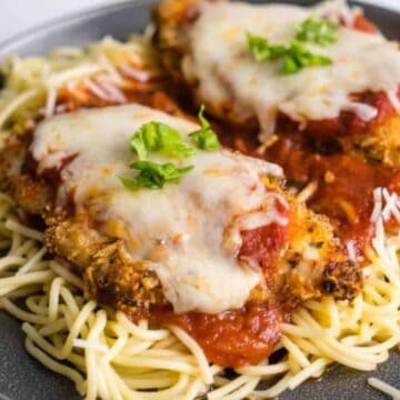 Chicken Parmesan with melted cheese and tomato sauce served over spaghetti, garnished with fresh basil.