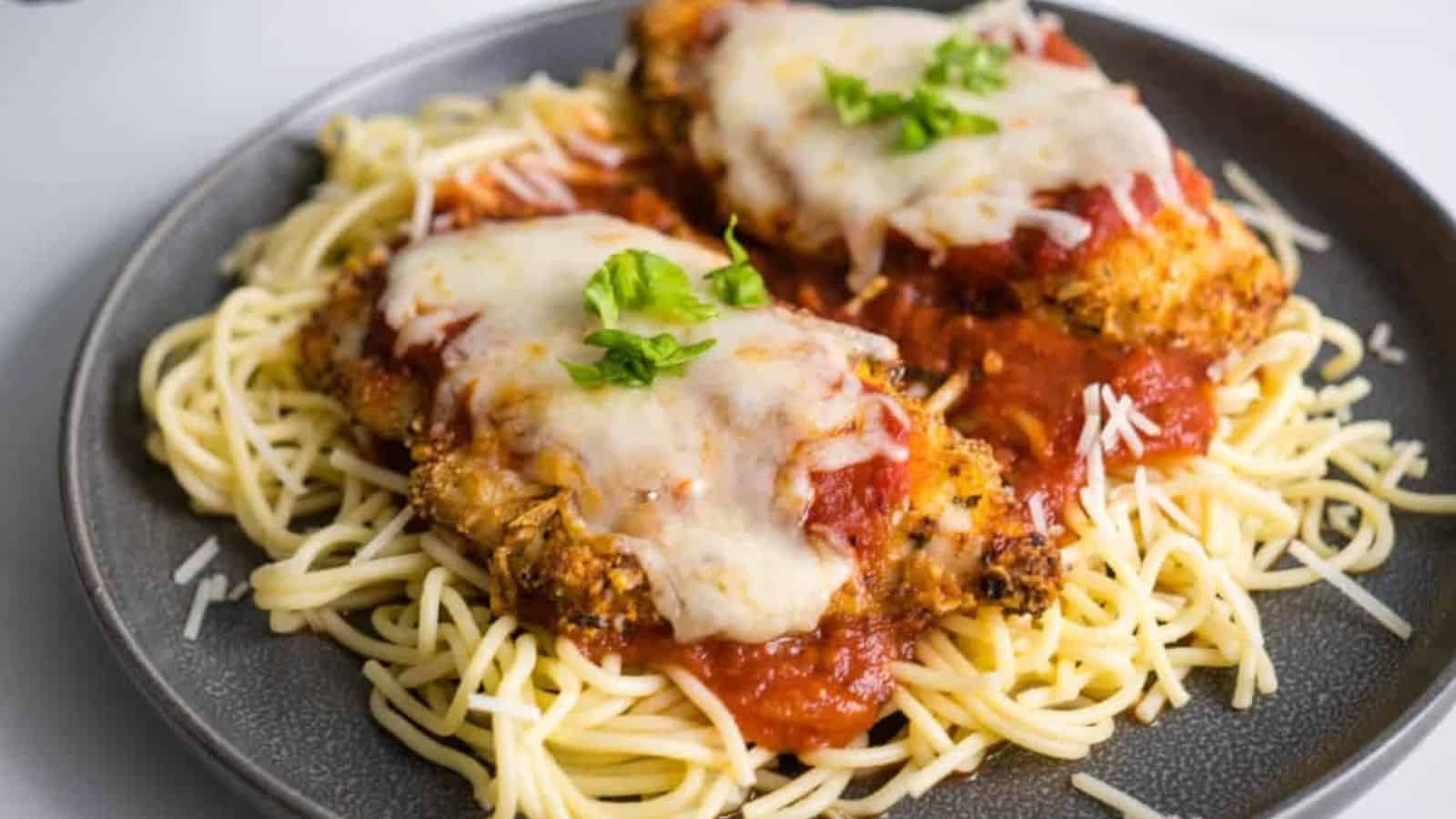 Chicken Parmesan with melted cheese and tomato sauce served over spaghetti, garnished with fresh basil.