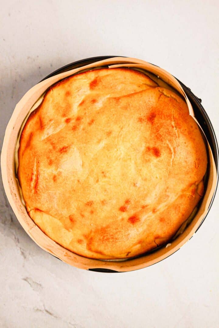 A golden, freshly baked Gluten Free Almond Eclair Cake in a round pan lined with parchment paper on a light surface.
