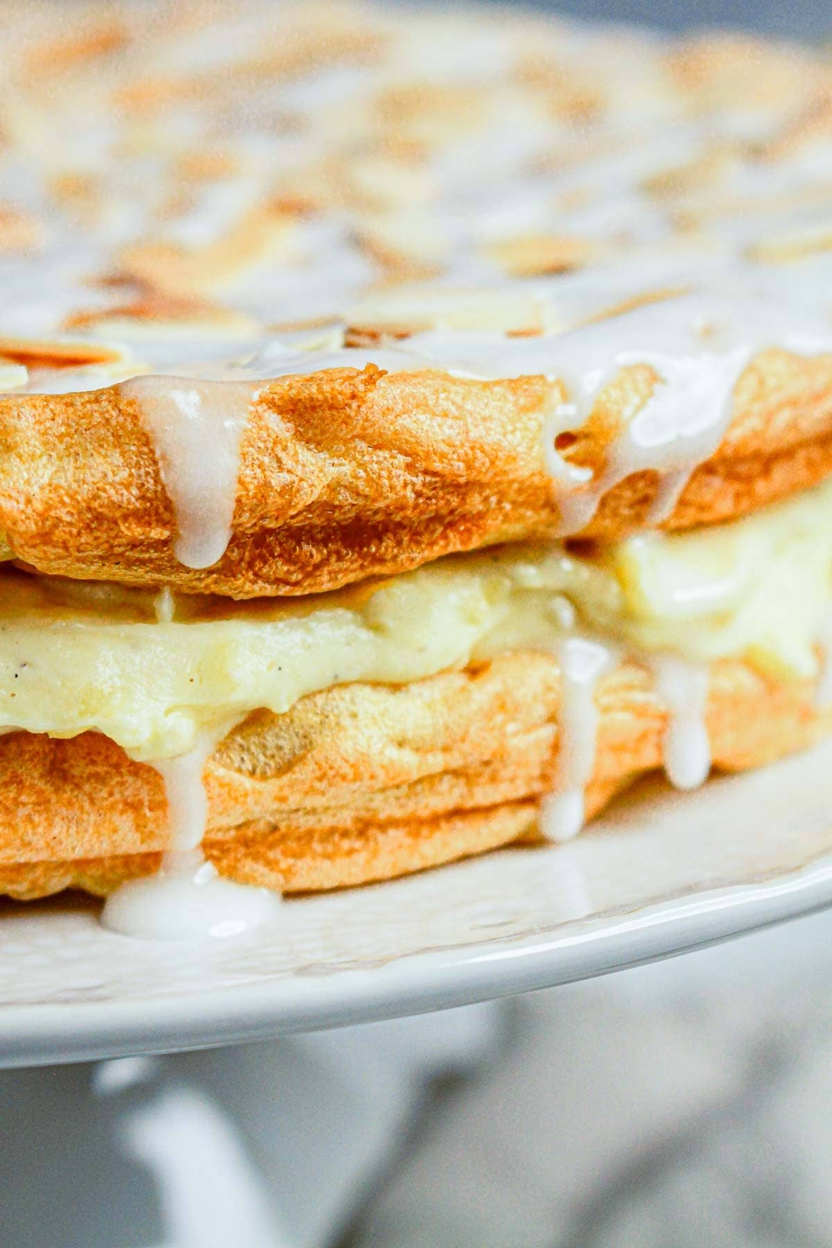 Close-up of layered waffles with creamy filling and white icing drizzled on top, reminiscent of a Gluten Free Almond Eclair Cake.