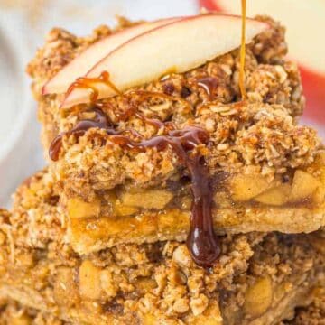 Three stacked apple crumble bars topped with a fresh apple slice, drizzled with caramel sauce.