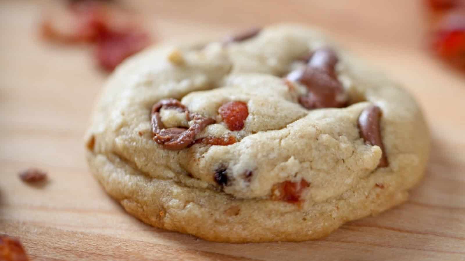 A cookie with bacon and chocolate chips on a wooden surface.